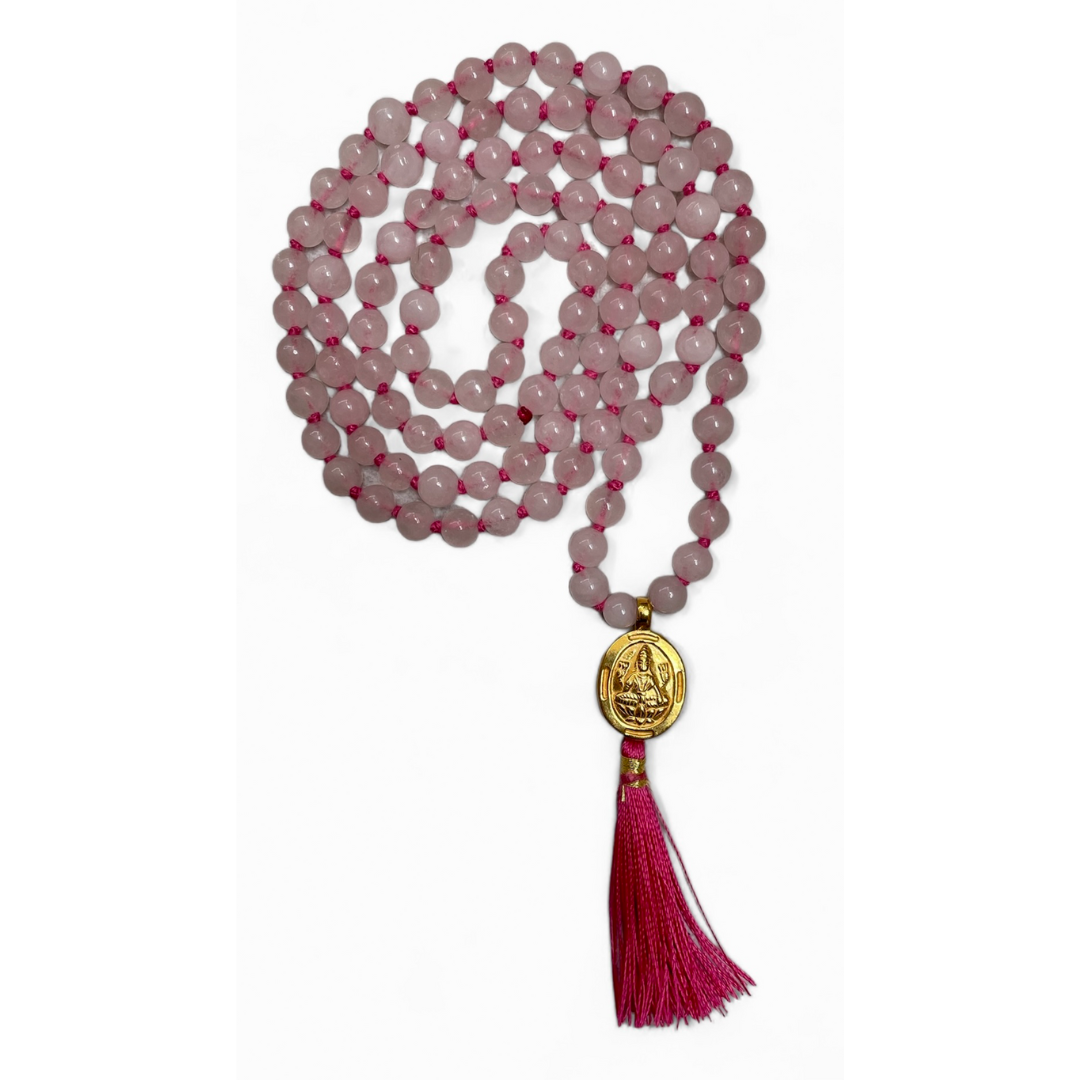 A pink rose quartz mala with a gold-plated Lakshmi charm and a red tassel at the end. The mala has 108 beads and a guru bead.