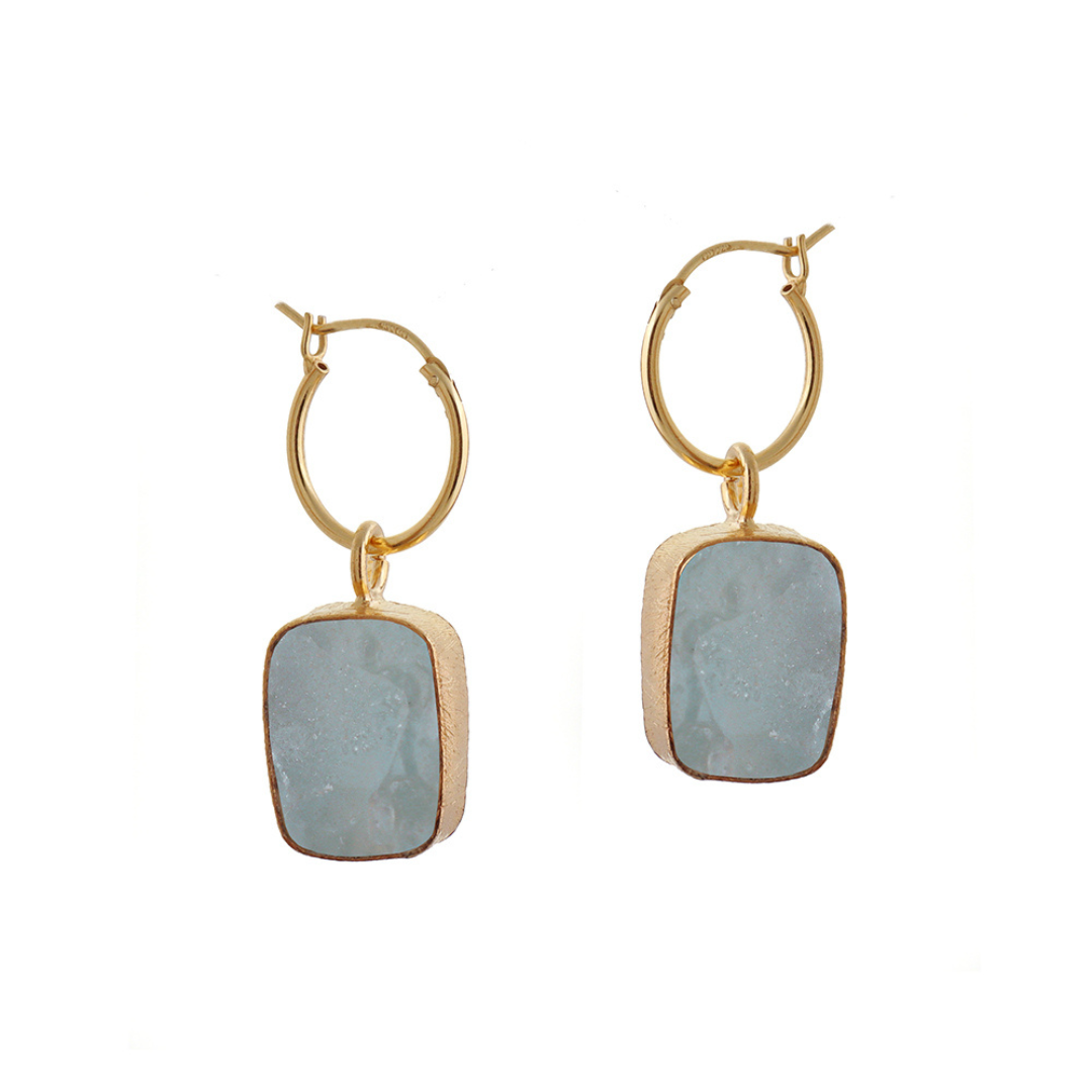 A pair of gold hoop earrings with rectangle raw blue aquamarine crystal pendants.